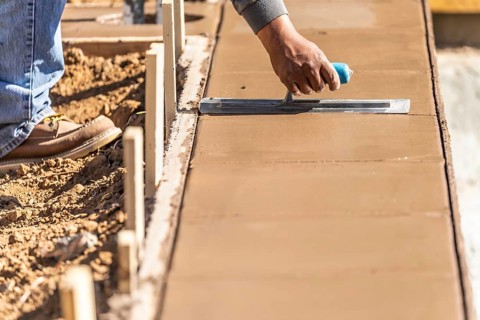 Construction worker using trowel on wet cement forming coping around new pool