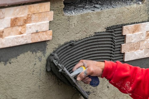 Worker installing wall tile cement with trowel and tile at construction site