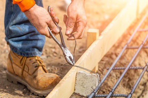 Worker securing steel rebar framing with wire plier cutter tool at construction site