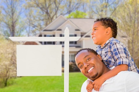 Happy african american father and mixed-race son in front of blank real estate sign and new house