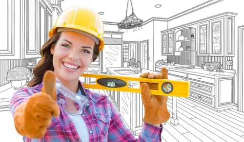 Female construction worker with thumbs up holding level in front of custom kitchen drawing