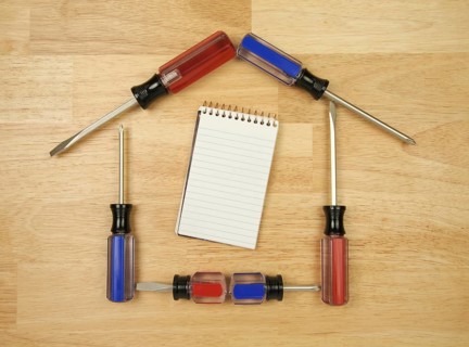 House shaped by screwdrivers and pad of paper on a wood background