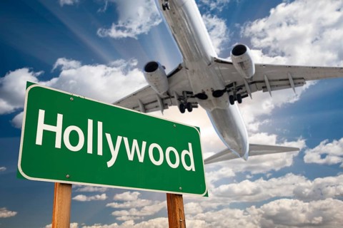 Hollywood green road sign and airplane above with dramatic blue sky and clouds