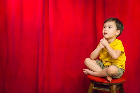 Handsome mixed-race boy sitting on stool in front of red curtain
