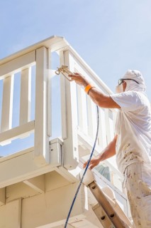 House painter wearing facial protection spray painting A deck of A home