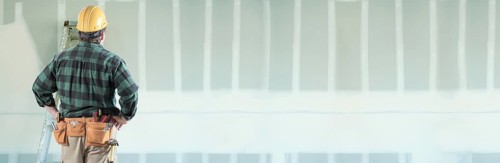 Male contractor wearing hard hat facing drywall banner background with ladder
