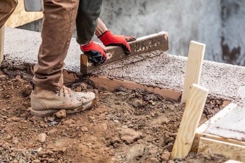 Construction worker leveling wet cement into wood framing