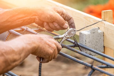 Worker securing steel rebar framing with wire plier cutter tool at construction site