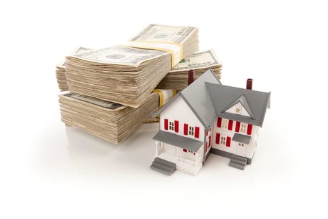 Small house with stacks of hundred dollar bills isolated on a white background