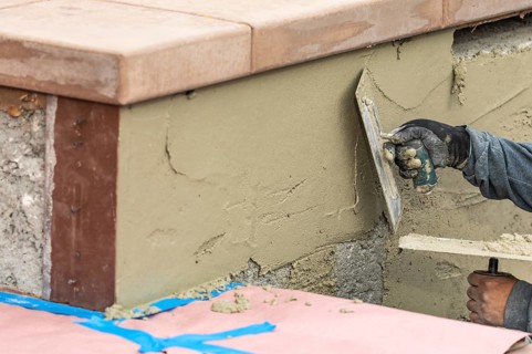 Tile worker applying cement with trowel at pool construction site