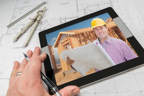 Hand of architect on computer tablet showing contractor and home framing photo over house plans