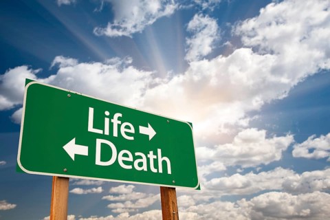 Life and death green road sign with dramatic clouds and sky