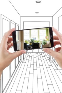Hand holding smart phone displaying photo of the house hallway drawing behind