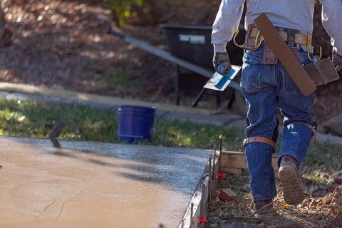 Construction worker with trowel tools near wet deck cement