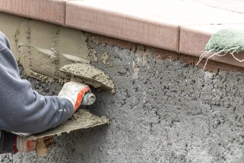 Tile worker applying cement with trowel at pool construction site
