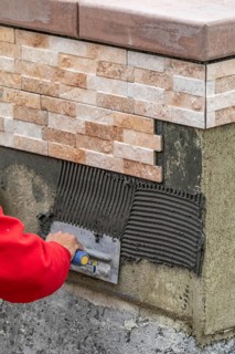 Worker installing wall tile cement with trowel and tile at construction site