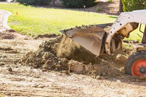 Small bulldozer digging in yard for pool installation