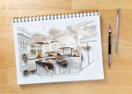 Sketch pad on desk with drawing of custom kitchen and brush stroke showing finished construction next to engineering pencil and ruler scale