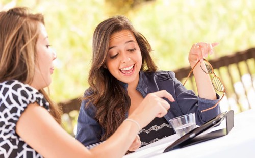Expressive young adult girlfriends using their computer electronics outdoors