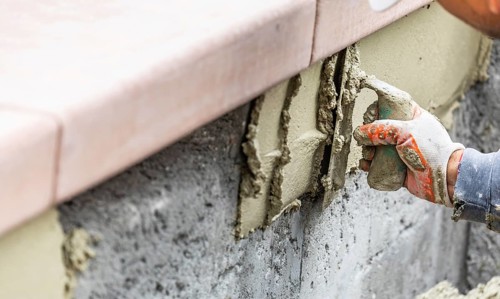 Tile worker applying cement with trowel at pool construction site