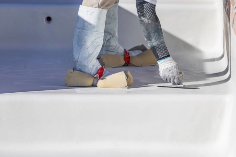 Worker wearing sponges on shoes smoothing wet pool plaster with trowel
