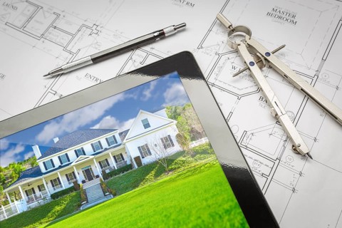 Computer tablet showing finished house sitting on house plans with pencil and compass