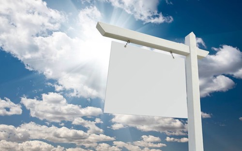 Blank real estate sign over clouds and blue sky with sun rays