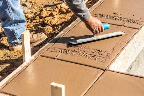 Construction worker using trowel on wet cement forming coping around new pool