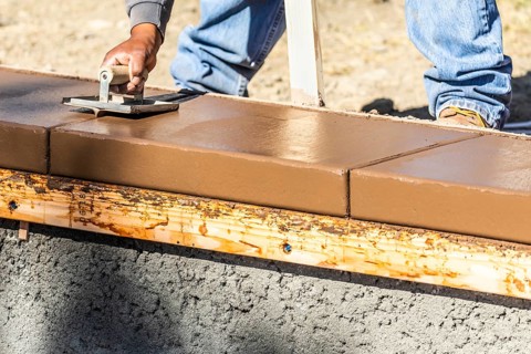 Construction worker using hand groover on wet cement forming coping around new pool