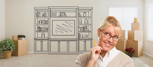 Woman inside room with moving boxes glancing toward entertainment unit drawing on wall