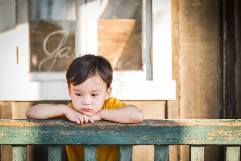 Melancholy mixed-race boy leaning on porch railing
