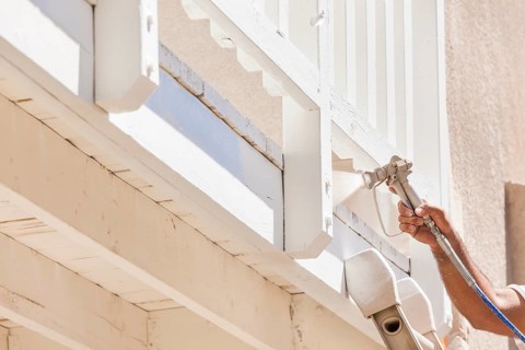 House painter wearing facial protection spray painting A deck of A home