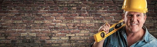 Male contractor in hard hat holding level in front of old brick wall banner with copy space