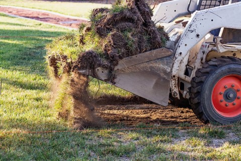 Small bulldozer removing grass from yard preparing for pool installation