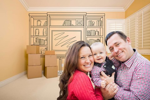 Young family in room with moving boxes and drawing of entertainment unit on wall