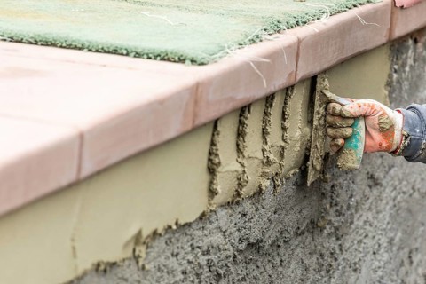 Tile worker applying cement with trowel at pool construction site