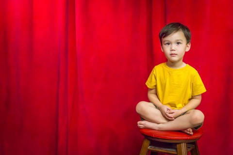 Handsome mixed-race boy sitting on stool in front of red curtain