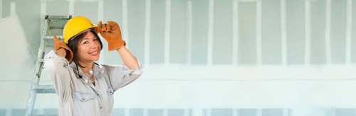 Hispanic female contractor wearing hard hat against drywall banner background with ladder