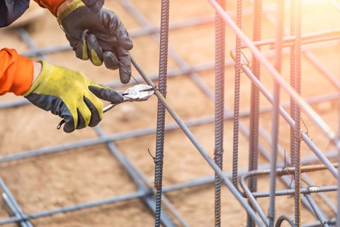 Worker securing steel rebar framing with wire plier cutter tool at construction site