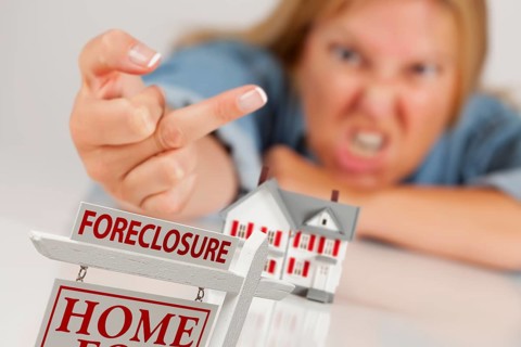 Angry woman flipping the bird behind model home and foreclosure real estate sign in front