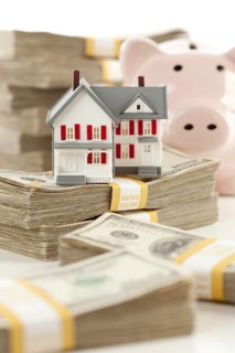 Small house and piggy bank with stacks of hundred dollar bills isolated on a white background