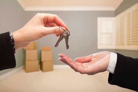 Woman handing over the house keys to A new home inside empty grey colored room