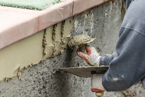 Tile worker applying cement with trowel at pool construction site