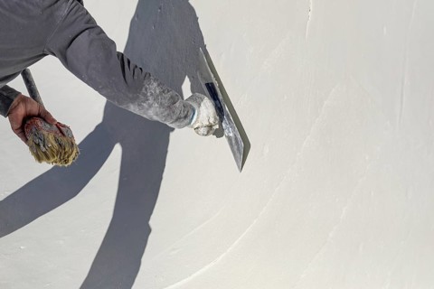 Worker smoothing wet pool plaster with trowel