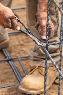 Worker securing steel rebar framing with wire plier cutter tool at construction site