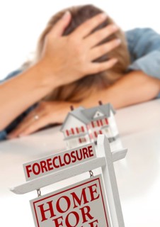 Woman with head in hand behind model home and foreclosure real estate sign in front