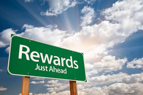 Rewards green road sign against clouds and sunburst
