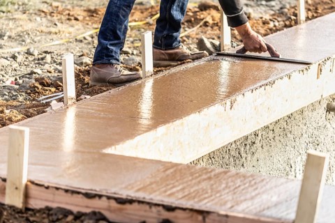 Construction worker using wood trowel on wet cement forming coping around new pool