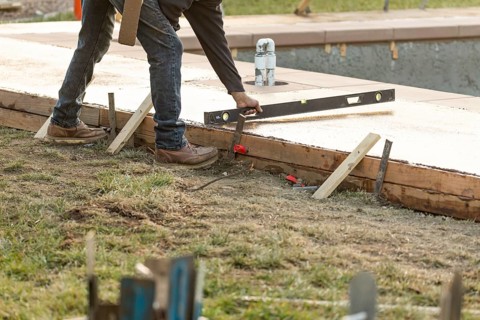 Construction worker checking level on wet deck cement