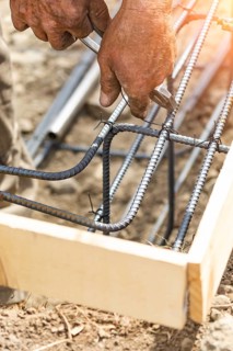Worker securing steel rebar framing with wire plier cutter tool at construction site